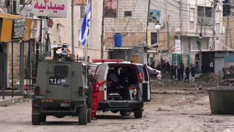 قوات الاحتلال الإسرائيلي توقف سيارة إسعاف فلسطينية للتفتيش أثناء إغلاقها طريقًا خلال مداهمة عسكرية في جنين بالضفة الغربية المحتلة، 22 يناير 2025
