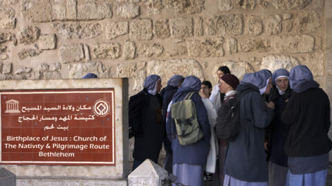 راهبات تقفن خارج مجمع كنيسة المهد في مدينة بيت لحم التاريخية في الضفة الغربية المحتلة، قبيل احتفالات عيد الميلاد. 22 ديسمبر/كانون الاول 2024.