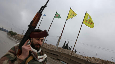 جندي من الجيش السوري يمرّ أمام أعلام وحدات حماية الشعب (YPG) المنصوبة على طول أحد شوارع الطبقة، في محافظة الرقة، على الضفة الجنوبية الغربية لنهر الفرات، في 18 يناير/كانون الثاني 2026.